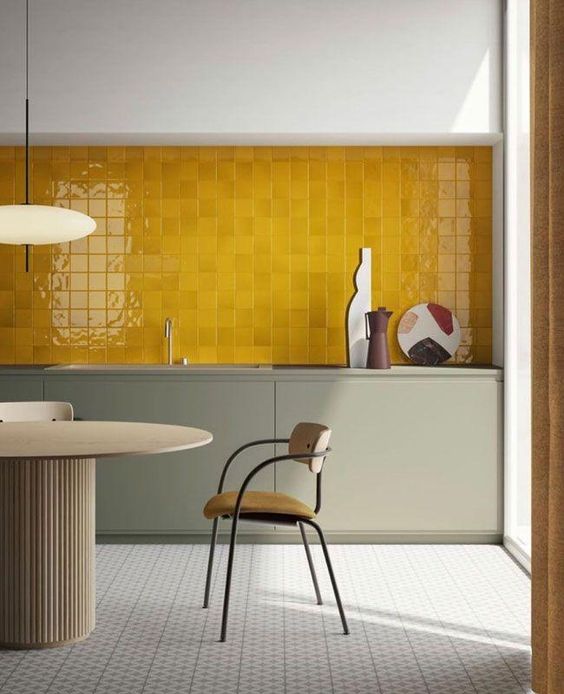 a sophisticated kitchen with gray base cabinets, an entire wall of juicy yellow tiles, elegant chairs and a table