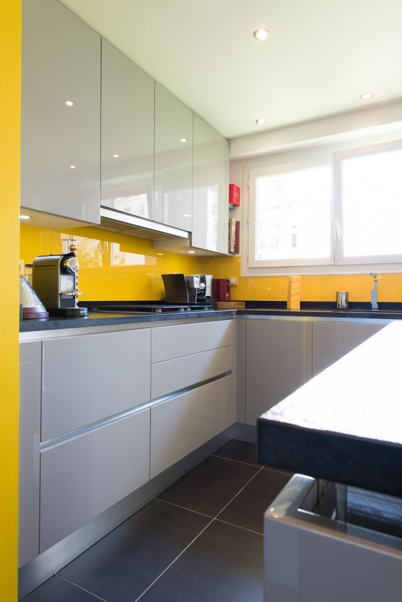 A stylish, minimalist kitchen with white and dove gray cabinets and a sunny yellow sleek glass backsplash stands out