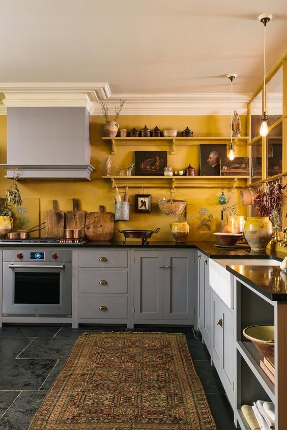 A vintage kitchen with gray cabinets, yellow walls, shelves with artwork and some vintage accessories is very elegant