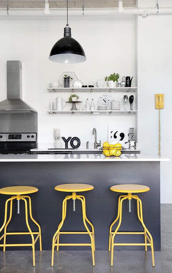 A white kitchen with graphite gray cabinets, bold yellow stools and other accents is complemented by a retro pendant light
