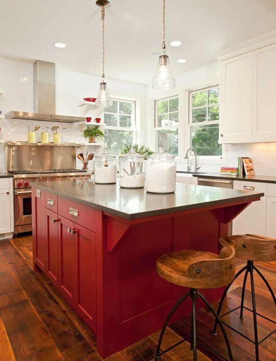 A beautiful vintage white kitchen with a red island, dark stone countertops and a metal stove with matching extractor hood