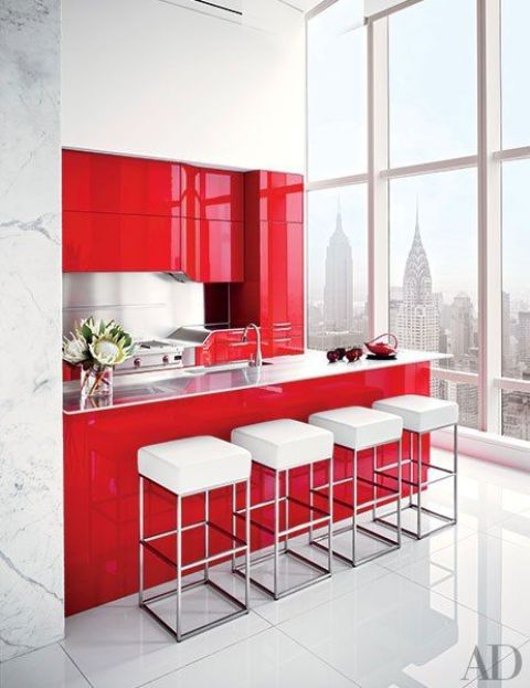 a bright, minimalist red and white kitchen with sleek metal splashbacks and worktops and a row of white stools