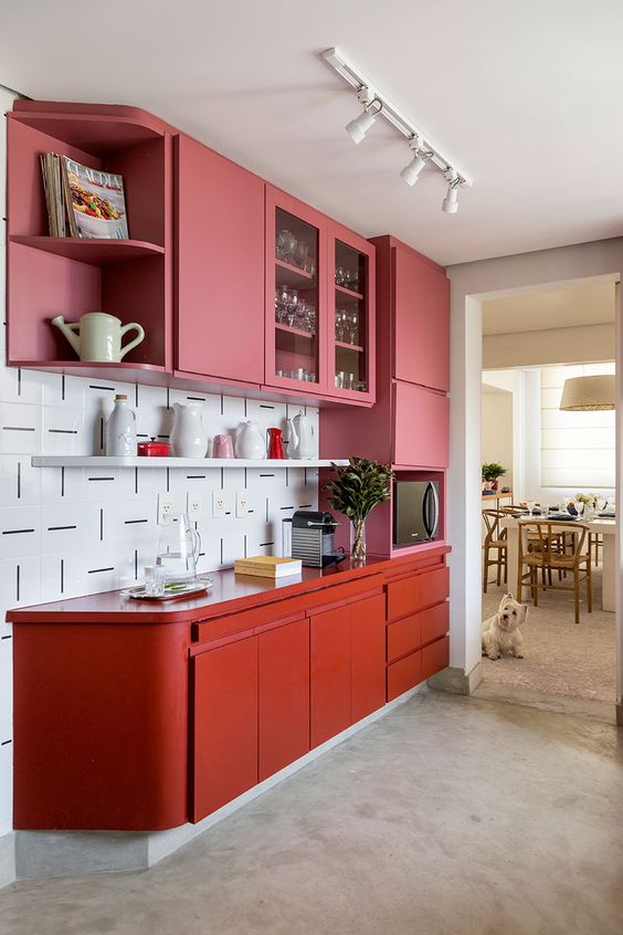 A colorful pink and red kitchen with sleek, handleless cabinets and a strikingly patterned white tile backsplash