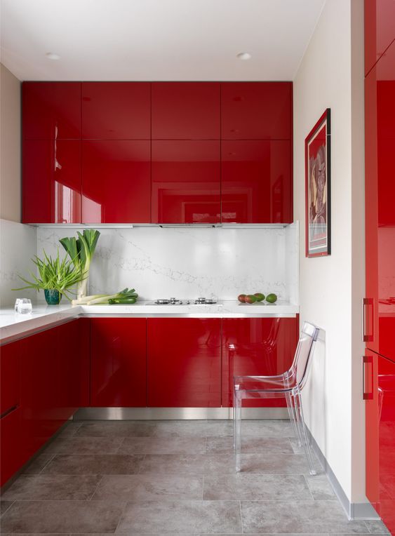 A minimalist deep red kitchen with a white stone backsplash and countertops, a transparent chair and a statement piece of artwork