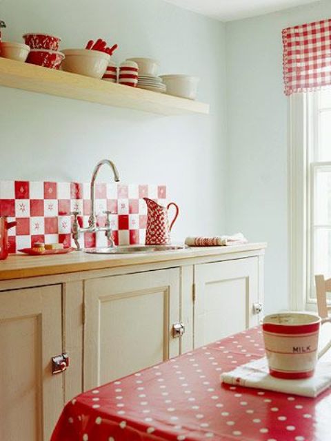 A neutral kitchen decorated in warm tones with a back wall made of red tiles, bed linen and textiles and bright red dishes looks cozy and old-fashioned