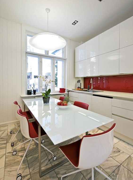 A sleek white kitchen with simple cabinets and an elegant red splashback and red chairs is a bold idea for a minimalism fan