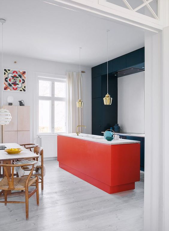 a stylish, modern kitchen with sleek navy blue cabinets and a red kitchen island, as well as white countertops and gold pendant lamps