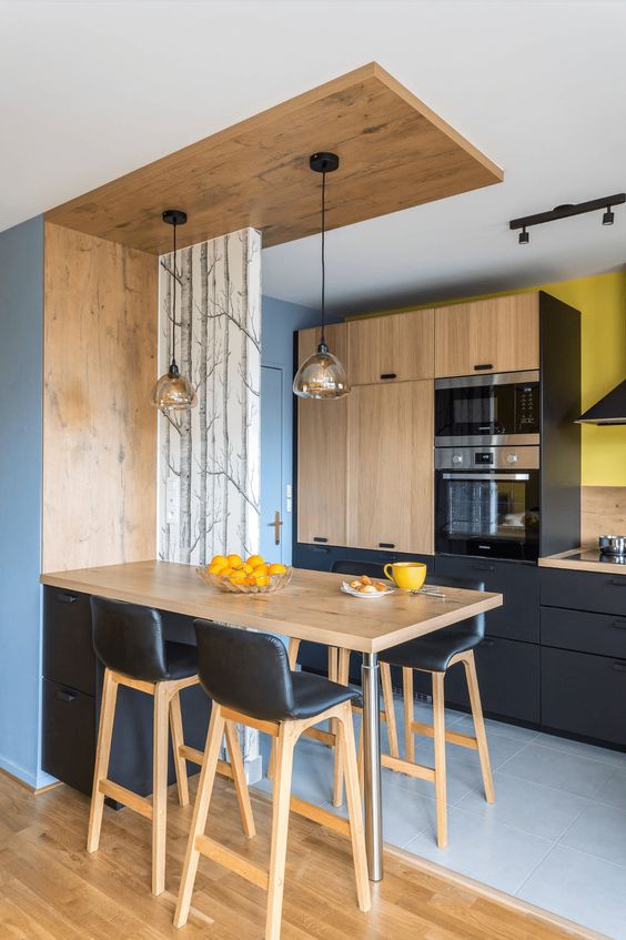 a modern black and light wood kitchen with pendant lamps, black leather stools and bright yellow accents