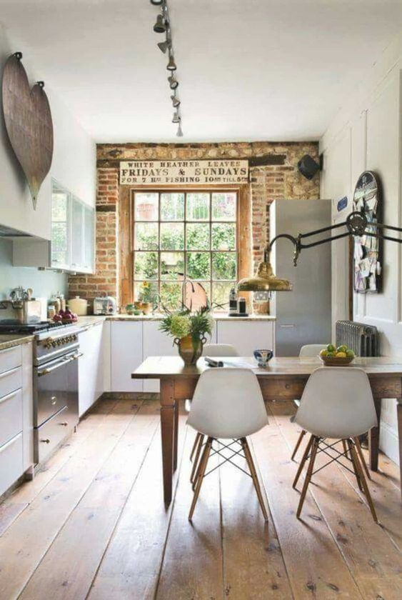 a country kitchen with white cabinets, stone countertops, a brick wall, metal appliances and a vintage wooden table and white chairs