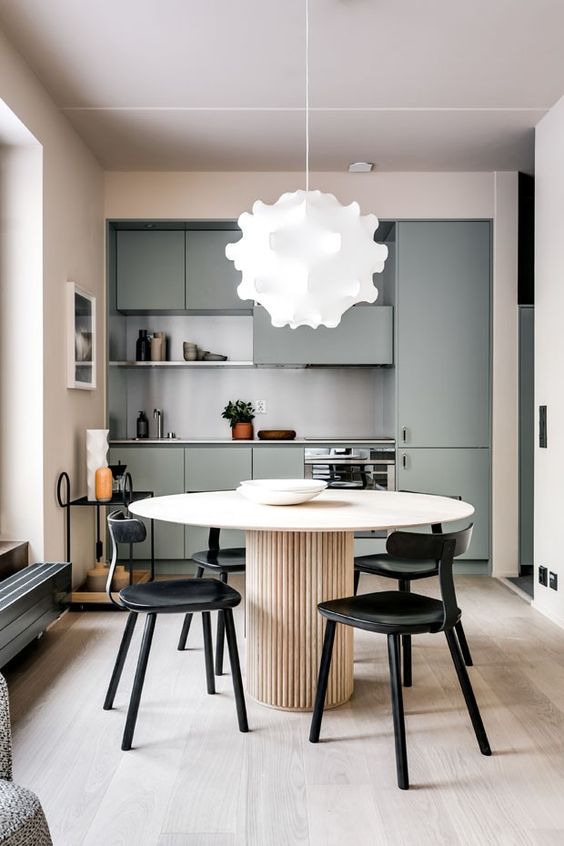a minimalist kitchen with green cabinets, a gray backsplash, a round wooden table and black chairs