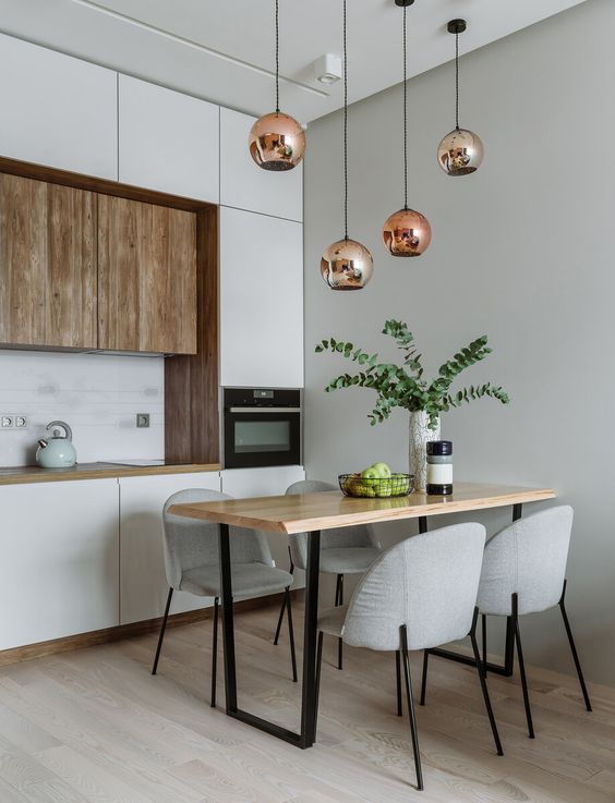 A minimalist kitchen with white and wooden cabinets, pendant lamps, a wooden table and gray chairs is very chic