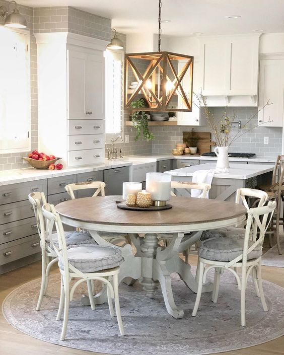a neutral farmhouse kitchen with gray and white cabinets, a hanging lamp, a large round wooden table and chairs