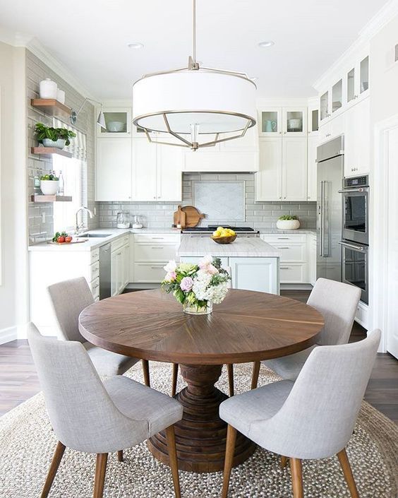 A neutral, modern farmhouse kitchen with a hanging lamp, round table and gray chairs is a very inviting space