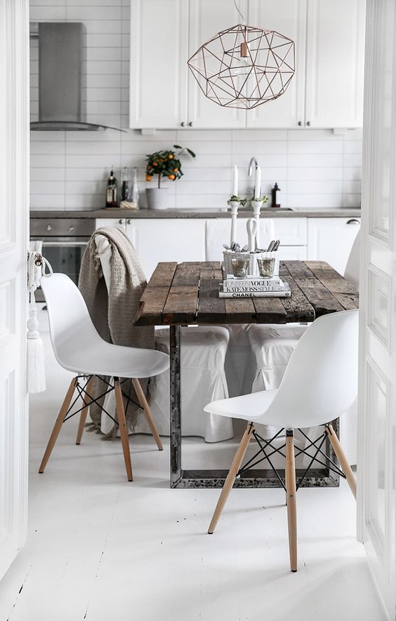 a Scandinavian kitchen in white with stone countertops, a metal hanging lamp, a rough wooden table and white chairs