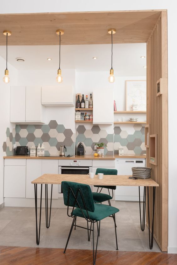 a stylish modern kitchen in white with gray, green and neutral hexagon tiles, green chairs and a small table with hairpin legs