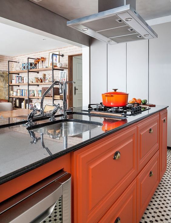 a bright, modern kitchen with orange cabinetry, black stone countertops and a metal hood, and vintage fittings