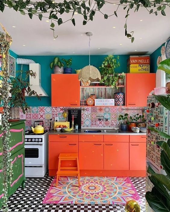 a colorful kitchen with orange cabinets, a mosaic tile floor and a colorful backsplash, teal walls and lots of plants