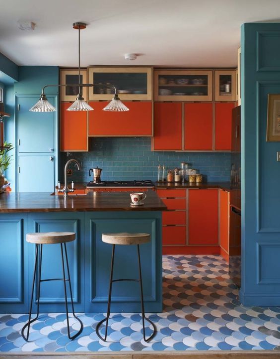 A colorful mid-century modern kitchen in blue and orange with dark stained wood countertops and vintage light fixtures