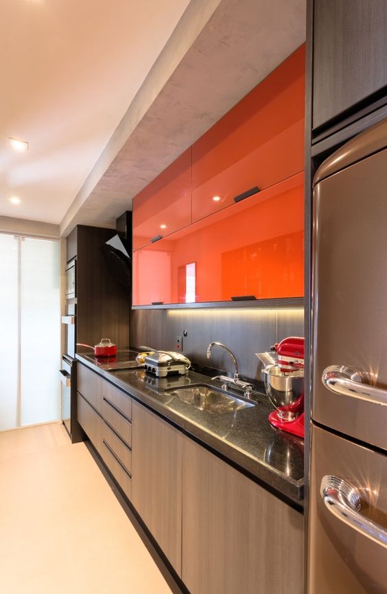 A modern, dark kitchen, spiced up with elegant upper cabinets and bright orange lights, looks dramatic