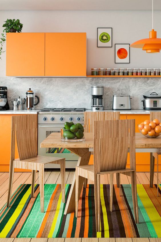 A super colorful kitchen with sleek orange cabinets, a marble backsplash and countertop, stained dining room furniture and a colorful rug