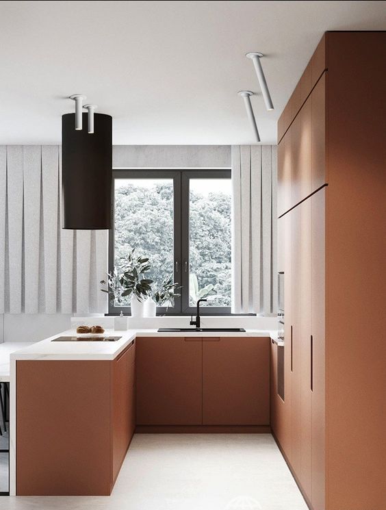 A very chic minimalist matt terracotta kitchen with white stone worktops and a black extractor hood and fittings is wow
