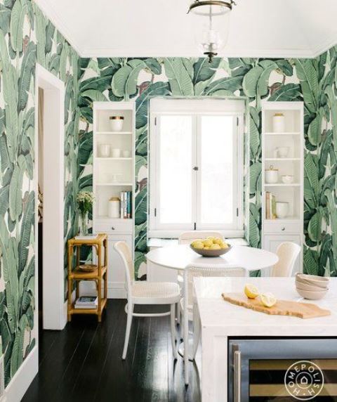 a bold tropical kitchen with banana leaf wallpaper, white furniture and a dining set with rattan chairs