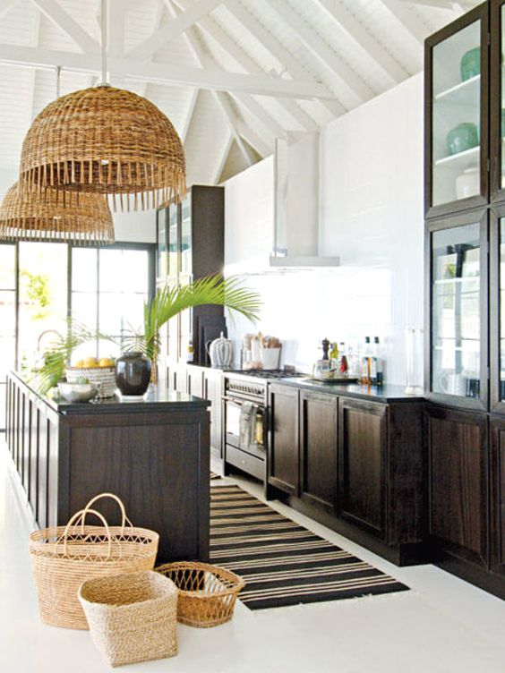 a bold tropical kitchen with white walls, dark-stained cabinets, woven pendant lights and baskets, and tropical foliage