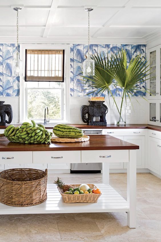 a bright and inviting tropical kitchen with blue tropical leaf wallpaper, white subway tiles and cabinets and baskets