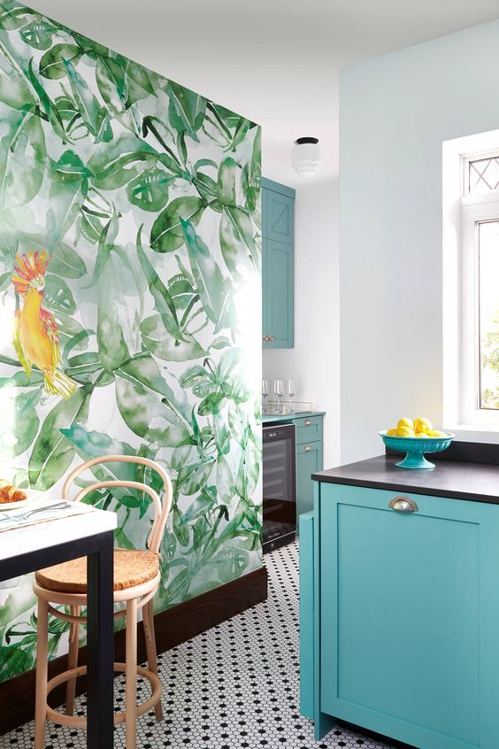 A colorful kitchen with a tropical mural, turquoise cabinets, dark appliances, and woven stools looks very tropical