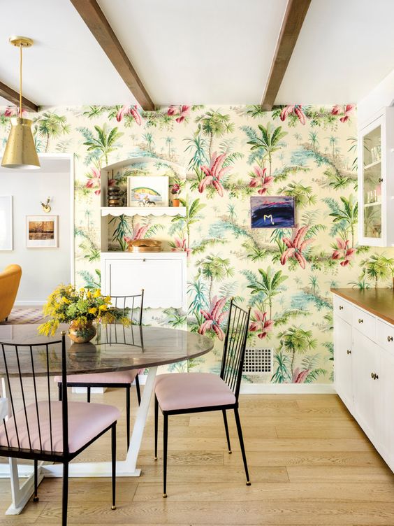 A colorful tropical kitchen with bright printed wallpaper, white cabinets, a round table, and pink chairs is fun and cool