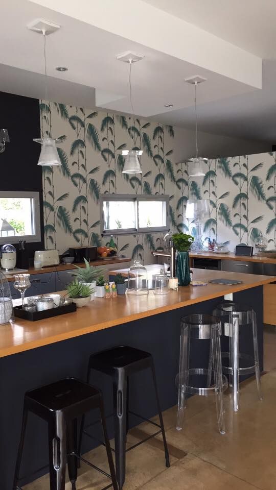 a laconic tropical kitchen with tropical wallpaper, gray cabinets and a black kitchen island, wooden countertops and pendant lamps