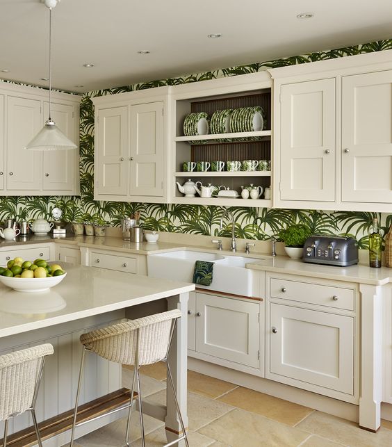 a neutral farmhouse kitchen with cream cabinets, tropical pattern wallpaper, cream looms and pendant lamps