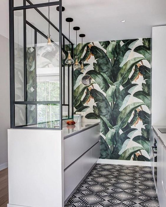 a stylish tropical kitchen with a banana leaf wall, white sleek cabinets, a mosaic floor and pendant lamps