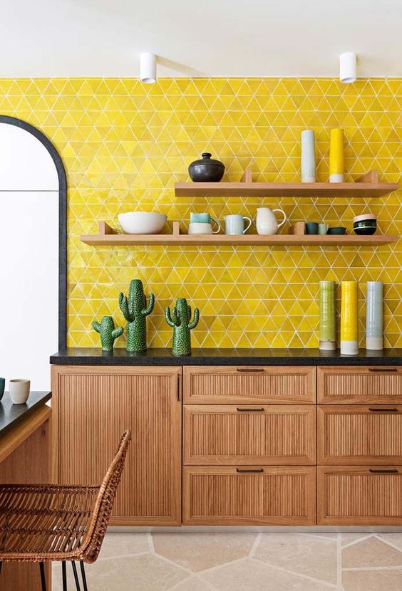 A mid-century modern kitchen with wooden cabinets and black countertops and lemon yellow tiles on the wall