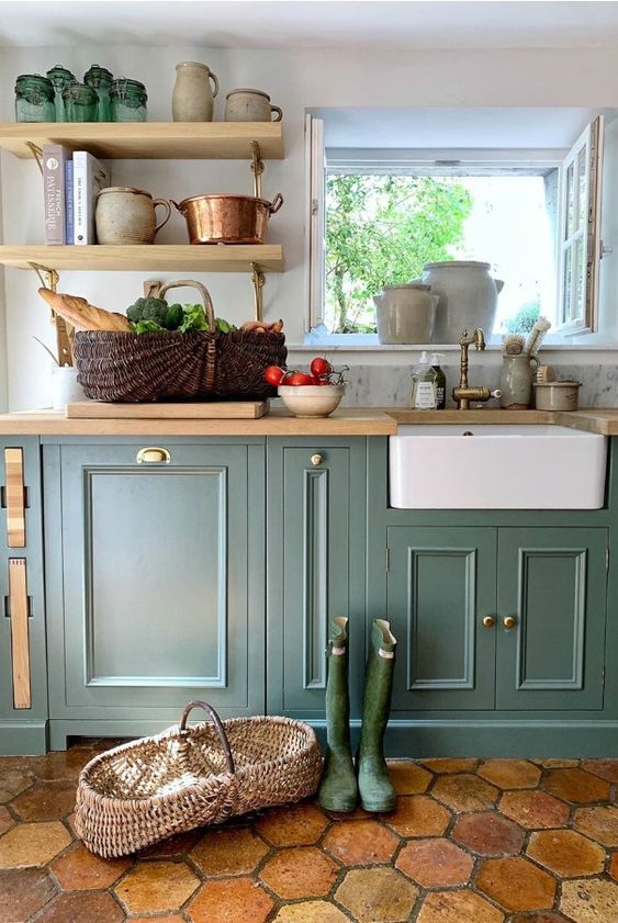 a French farmhouse kitchen with dark green cabinets, butcher block countertops and matching shelves, and tile flooring