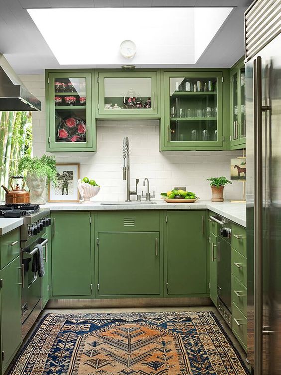 A mid-century modern green kitchen with a skylight, white tile backsplash and white countertops, and a printed rug