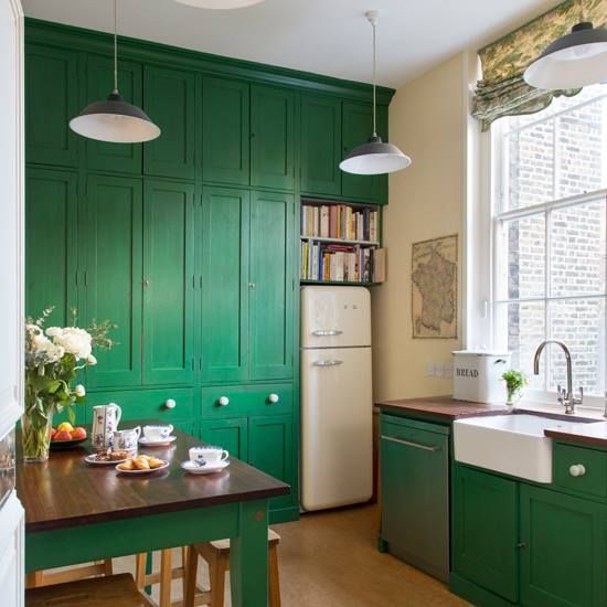 a pretty emerald green kitchen with dark stained wood countertops, pendant lamps and printed shades
