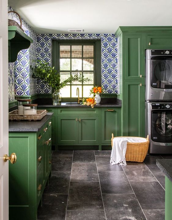 A green vintage kitchen with black countertops, light wallpapered walls and built-in washing machines