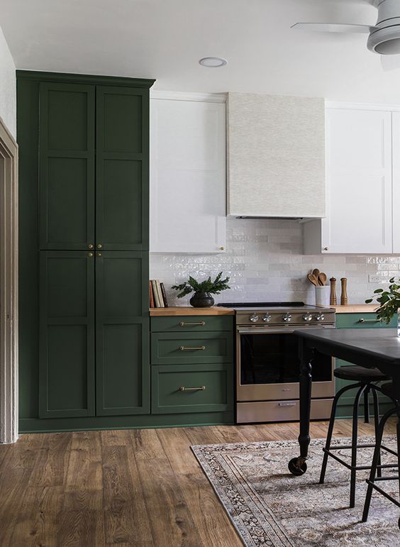 An eclectic hunter green kitchen with white upper cabinets, a subway tile backsplash and a white range hood