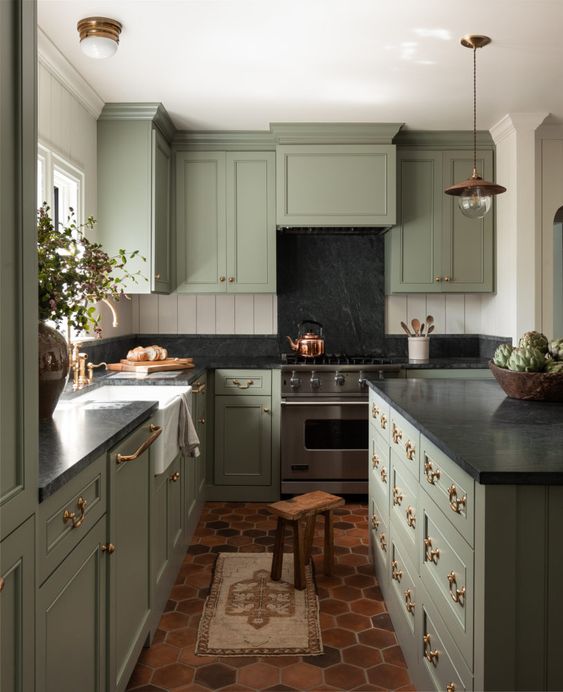 an English country kitchen in pale green, with black stone countertops and brass and copper accents
