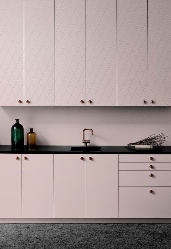A chic pale pink kitchen with patterned and sleek cabinets and black countertops for a bold contrast