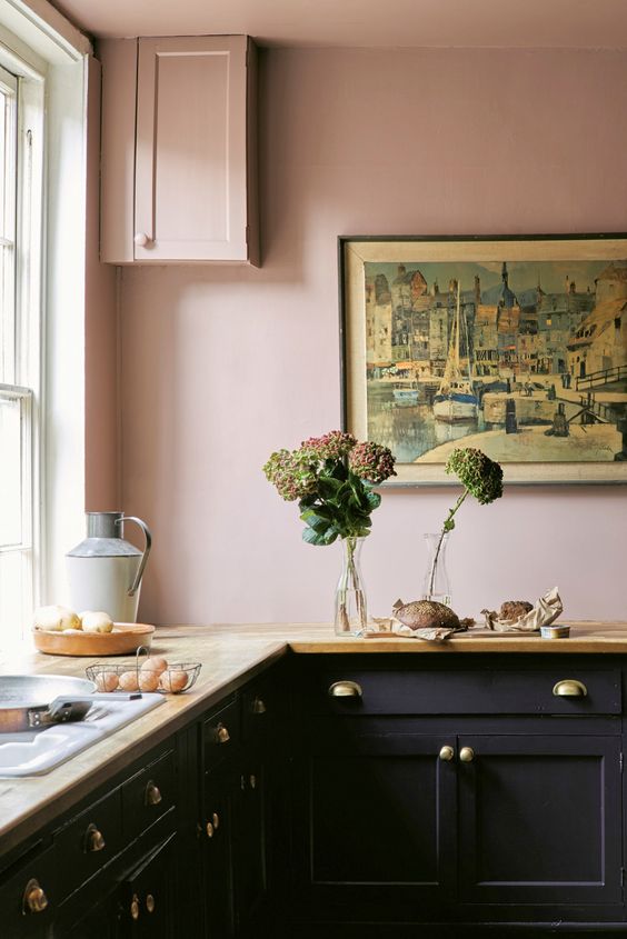 a vintage-inspired kitchen with blush walls, black cabinets, butcher block countertops and gold handles, and eye-catching artwork