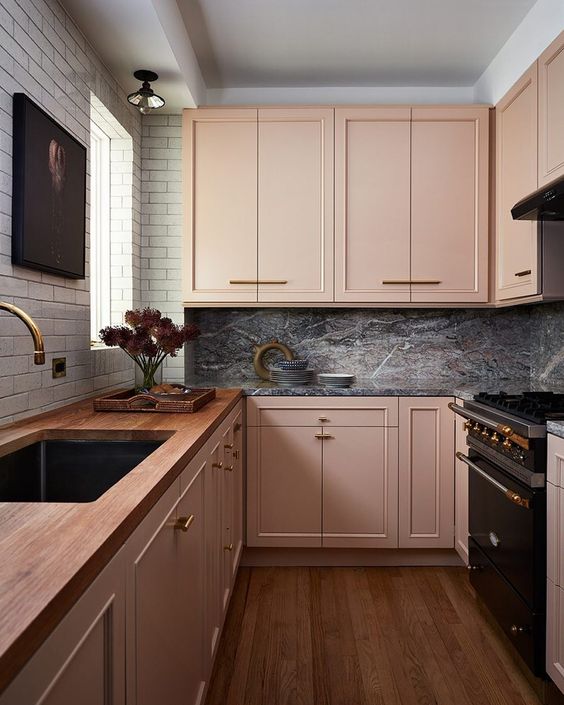 an eclectic kitchen with blush cabinets, a white tile wall, a gray marble backsplash, and dark appliances