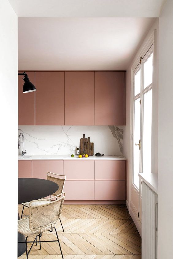 An ultra-minimal dusty pink kitchen with sleek cabinets, a white marble backsplash and countertops, and black accents