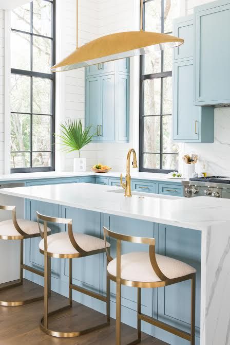 a beautiful light blue kitchen with white marble countertops and a backsplash and gold and brass accents