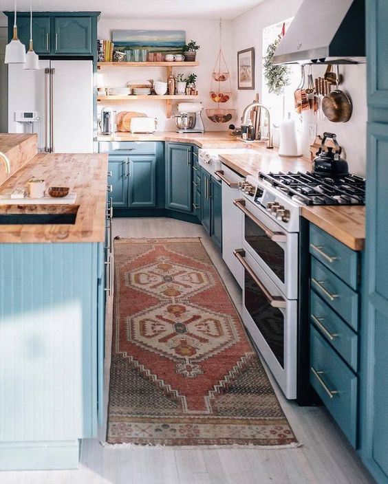 a blue farmhouse kitchen with wooden worktops, a white splashback and hanging lamps