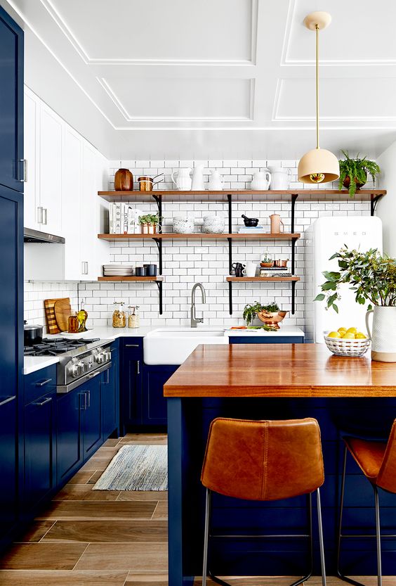A classic blue kitchen with a white subway tile backsplash, white countertops and open wooden shelves