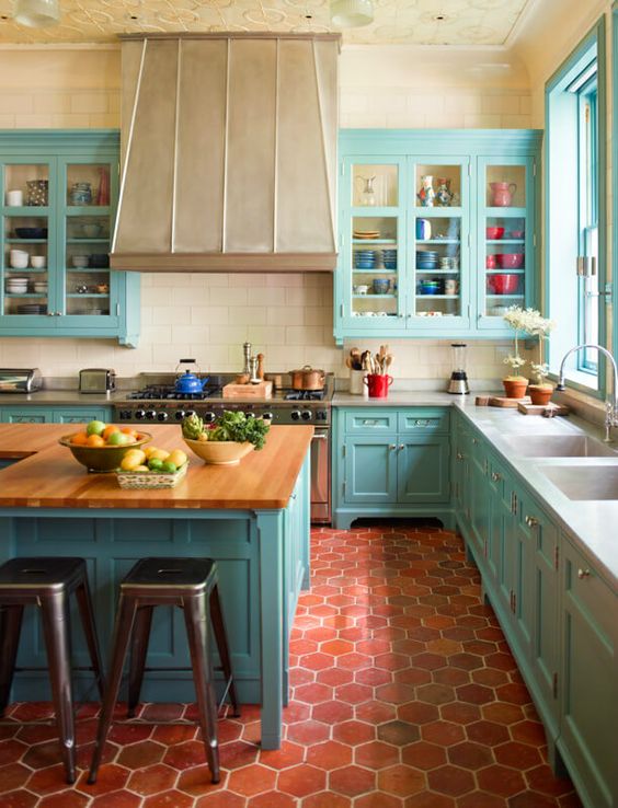 a light blue vintage-style kitchen with neutral countertops, a large hood and kitchen island, and metal stools