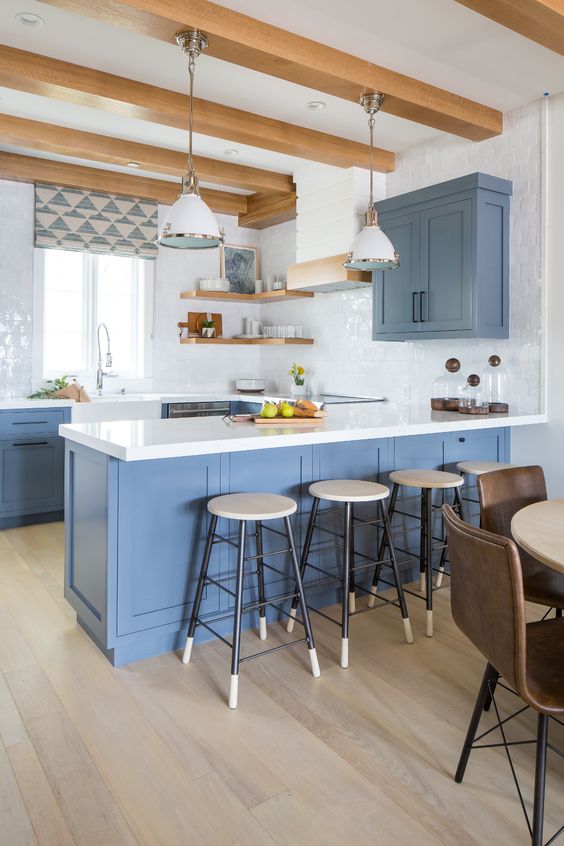 A light blue kitchen with white stone countertops and a white tile backsplash, open shelves and wooden beams looks inviting