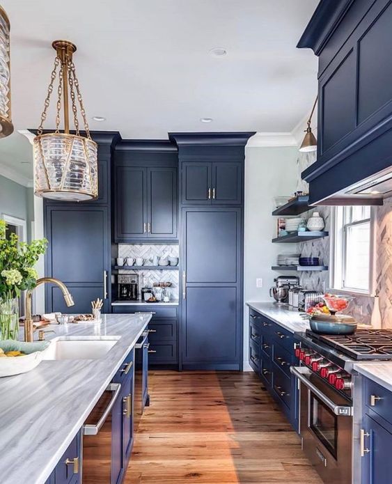 A striking blue kitchen with a marble tile backsplash, stone countertops and statement pendant lamps and sconces